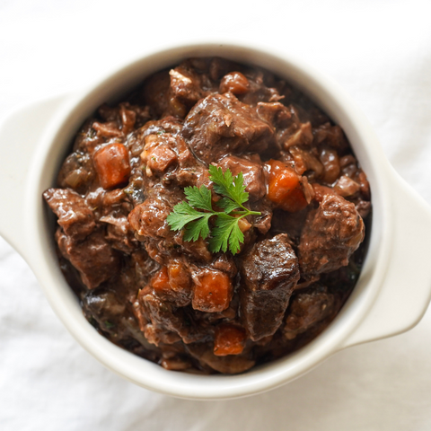 Bowl of beef stew with carrots and parsley on a white background