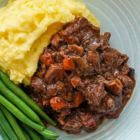 Beef stew with mashed potatoes and green beans on a blue plate