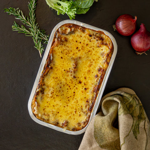 Baked dish in a metal tray on a dark surface with herbs and onions.