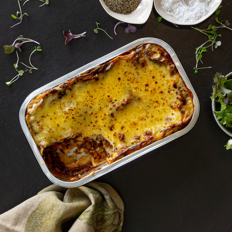 Baked dish in a rectangular tin on a dark surface with herbs and a towel.