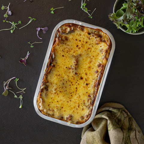 Baked dish in a rectangular metal tray on a dark surface with microgreens around