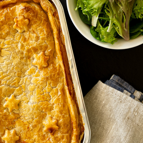 Baked dish with star-shaped crust next to a bowl of salad on a dark surface.