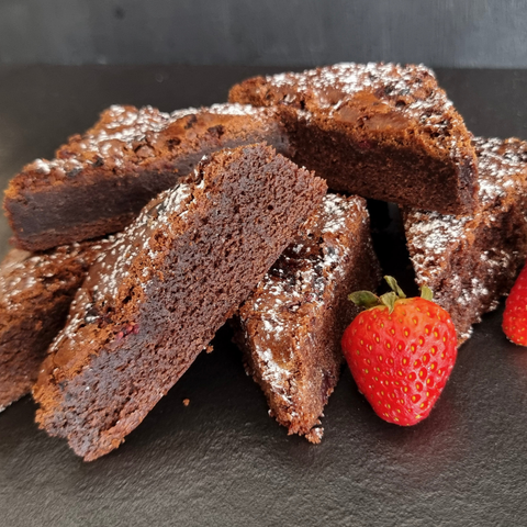 Chocolate brownies with powdered sugar on a dark surface with strawberries.