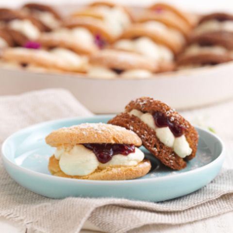 Two jelly-filled cookies on a blue plate with a blurred background of more cookies.
