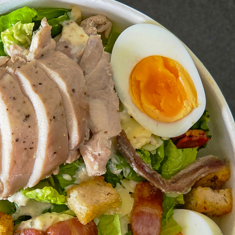 Salad with sliced chicken, boiled egg, bacon, and croutons on a bed of lettuce.