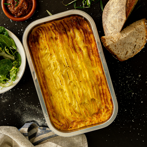 Shepherd's pie in a baking dish with bread and salad on a dark surface