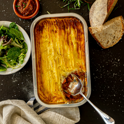 Shepherd's pie in a baking dish with a side of salad and bread on a dark surface