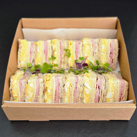 Box of assorted sandwiches with visible layers on a dark background
