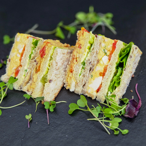 Triangular slices of a sandwich with vegetables on a dark surface with green herbs.