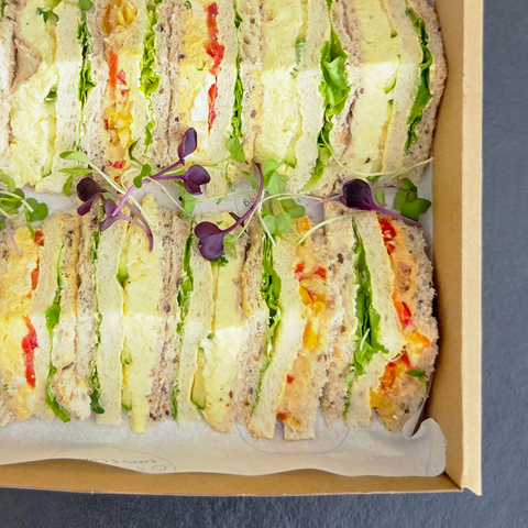 Box of sliced sandwiches with visible layers of vegetables on a blue background