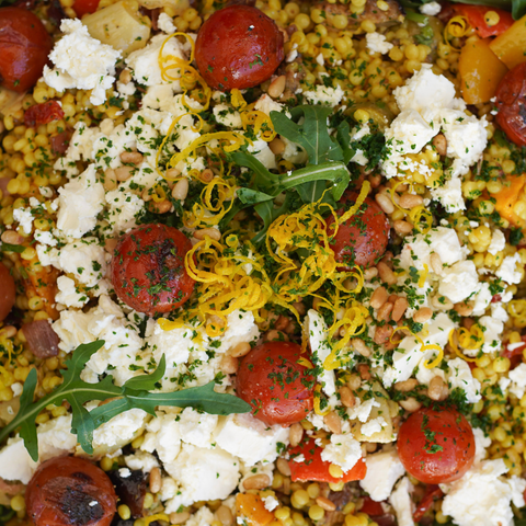 Colorful salad with tomatoes, feta cheese, and herbs on a bed of couscous.