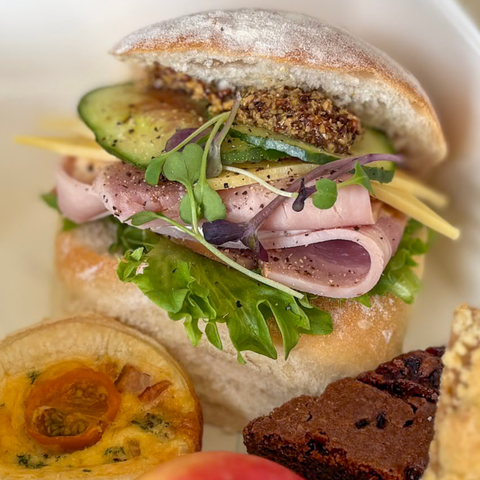 Close-up of a sandwich with ham, avocado, and vegetables on a white plate.