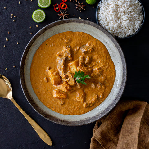 Bowl of curry with rice and garnishes on a dark surface