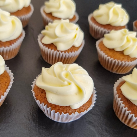 Row of cupcakes with white frosting on a dark surface