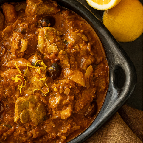 Spicy chicken dish with lemon zest in a black skillet on a wooden surface