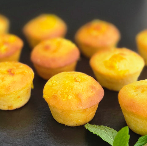 Small yellow muffins on a dark surface with a sprig of mint.