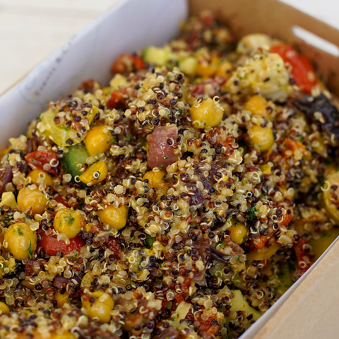 Colorful quinoa salad with chickpeas and vegetables in a cardboard container.