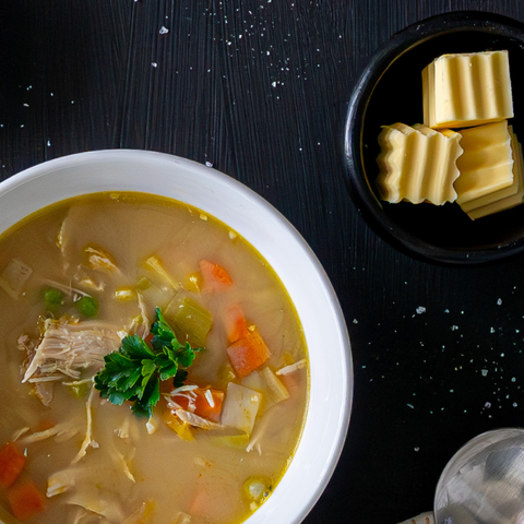 Vegetable soup in a white bowl with cheese slices on the side on a black surface