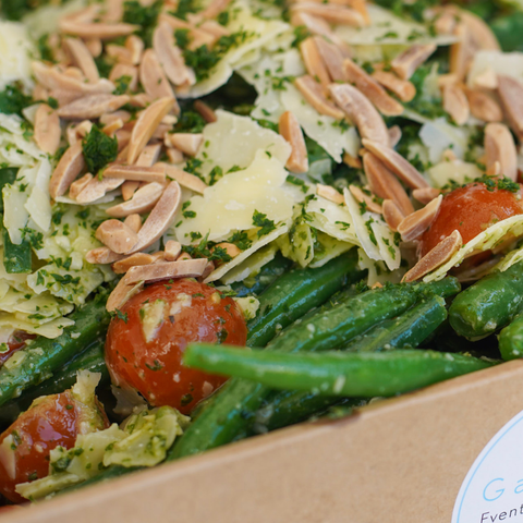 Close-up of a salad with greens, tomatoes, and almonds in a cardboard container.