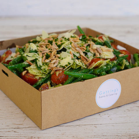Salad in a cardboard box with a 'Gattinger's Events & Catering' label on a wooden surface.