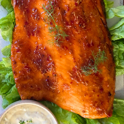Grilled salmon fillet on a bed of lettuce with a small bowl of sauce.