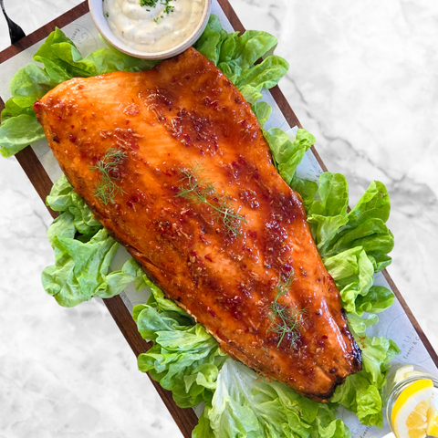 Grilled salmon fillet on a bed of lettuce with a side of sauce on a marble surface