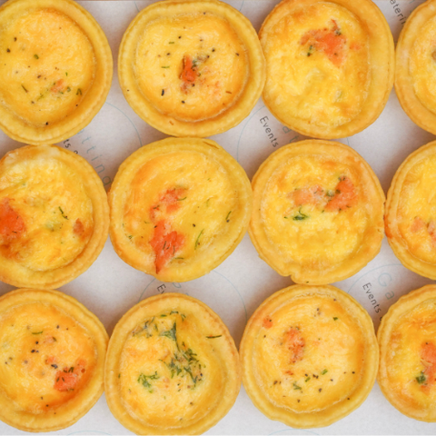 Row of small yellow quiches on a white surface