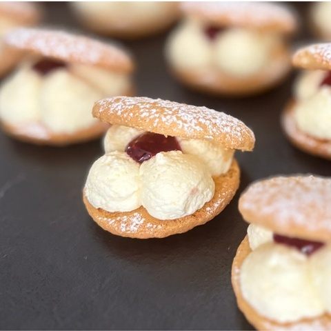 Small cookies with cream and jam filling on a dark surface
