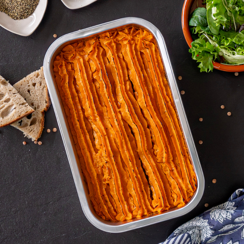 Shepherd's pie in a baking dish on a dark surface with bread and salad.