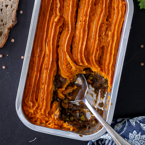 Shepherd's pie in a baking dish with a spoon, on a dark surface.