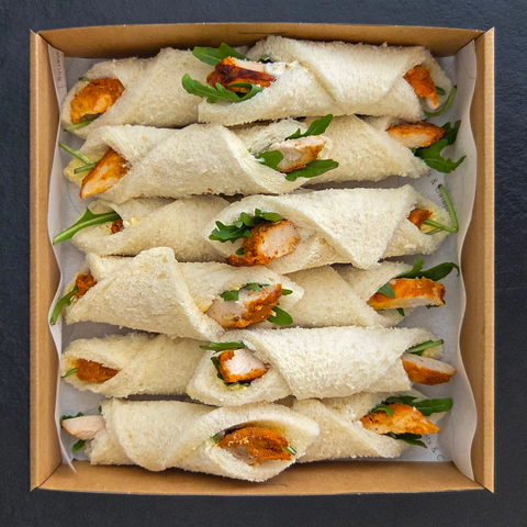 Box of small sandwiches with chicken and salad on a dark background