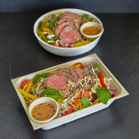 Plated salad with sliced meat and garnishes on a dark surface