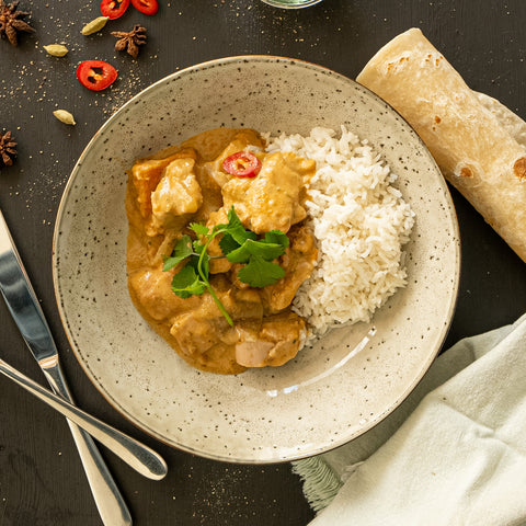Plated dish of chicken curry with rice and naan bread on a dark surface.