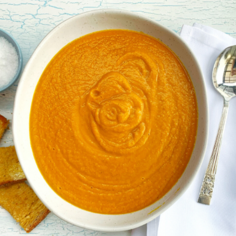  bowl of orange soup with a spoon and bread on a light blue surface