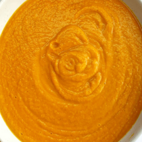 Close-up of orange hummus with a rose design on a white plate