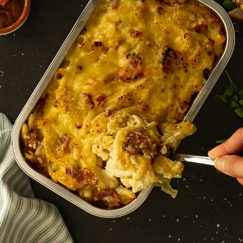 Macaroni and cheese dish being served from a metal tray on a dark surface.