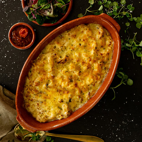 Baked dish in a terracotta dish with a side of salad on a dark surface